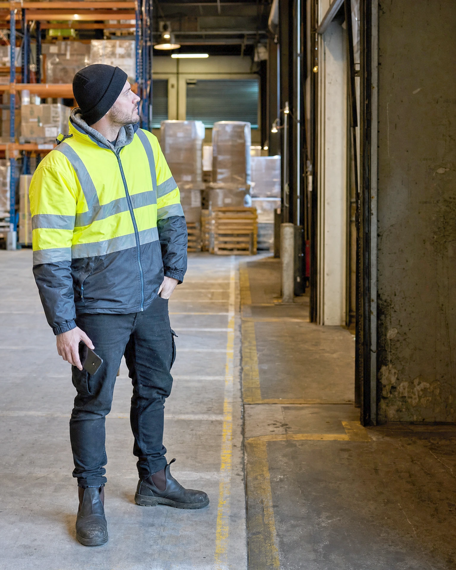 A warehouse worker in hi-vis pausing to inspect a loading-bay area during a shift